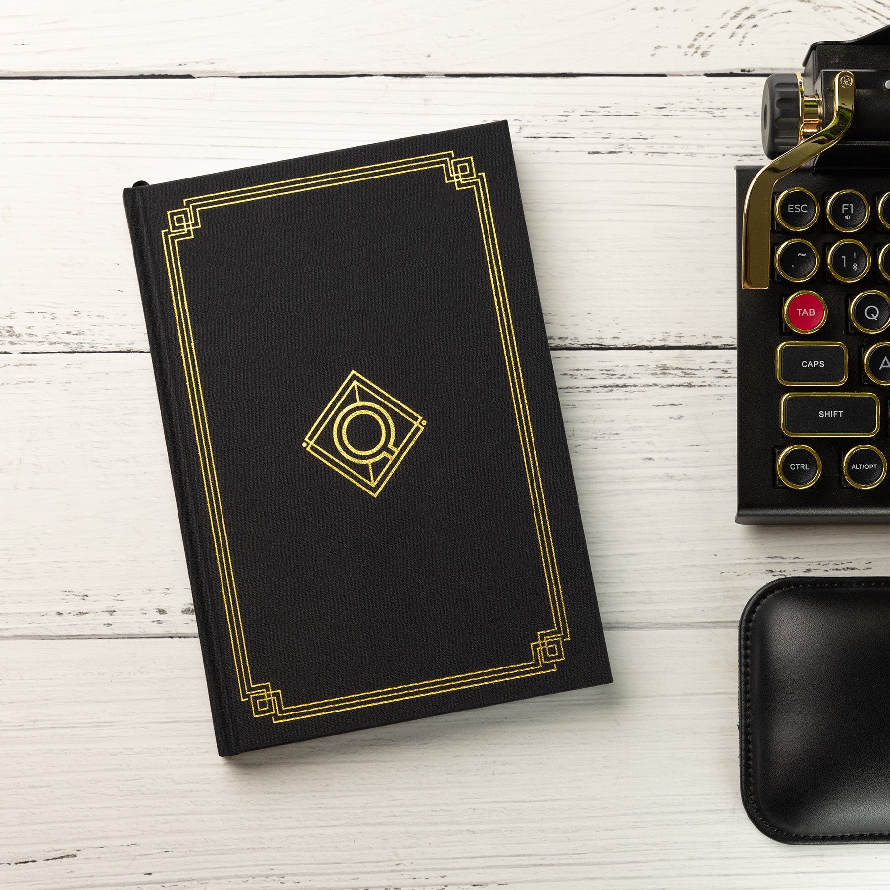 Qwerkywriter Official QWERKYTOYS Lined Journal in black gold and black chrome next to black gold qwerkywriter typewriter keyboard US ANSI layout 