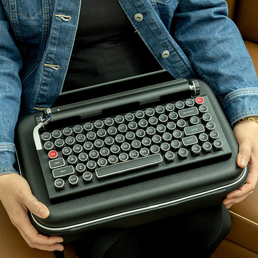 Qwerkywriter typewriter keyboard best in class premium all aluminum body in black chrome sitting with Qwerkywriter official carrying case on a wood bench