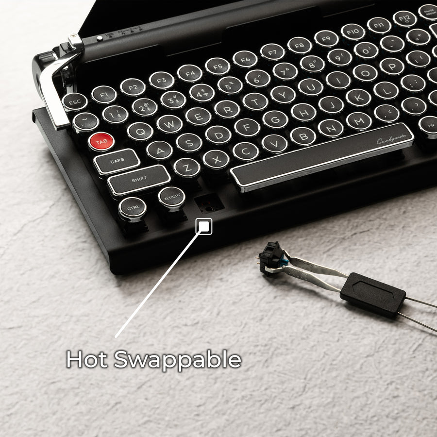Qwerkywriter typewriter keyboard best in class premium all aluminum body in black chrome on grey wood grain background with hot swap tool and cherry mx blue switch callout