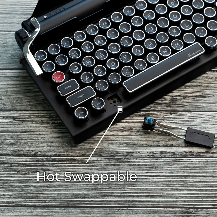 Qwerkywriter typewriter keyboard best in class premium all aluminum body in black chrome on grey wood grain background with hot swap tool and cherry mx blue switch callout