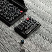 Qwerkywriter typewriter keyboard numkey numpad best in class premium all aluminum body in black chrome left view on grey wood grain with hot swap tool and cherry mx blue switch