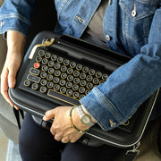 Qwerkywriter typewriter keyboard best in class premium all aluminum body in black chrome sitting with Qwerkywriter official carrying case sitting on chair