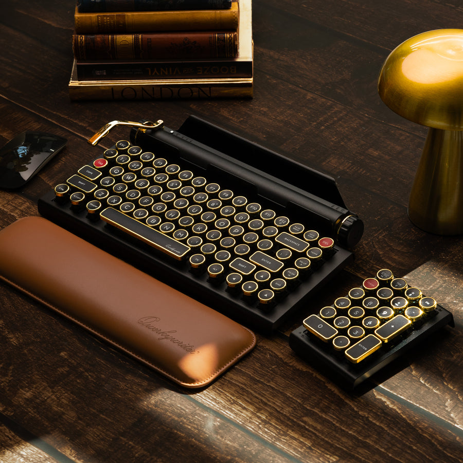 Qwerkywriter typewriter keyboard best in class premium all aluminum body in black gold hero image on brown wood grain background inside a library