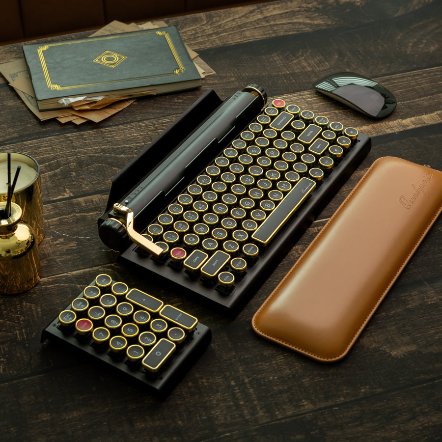 Qwerkywriter typewriter keyboard best in class premium all aluminum body in black gold hero image on brown wood grain background inside a library