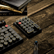 Qwerkywriter typewriter keyboard numkey numpad best in class premium all aluminum body in black gold close view on brown wood grain with hot swap tool cherry mx blue switch and books