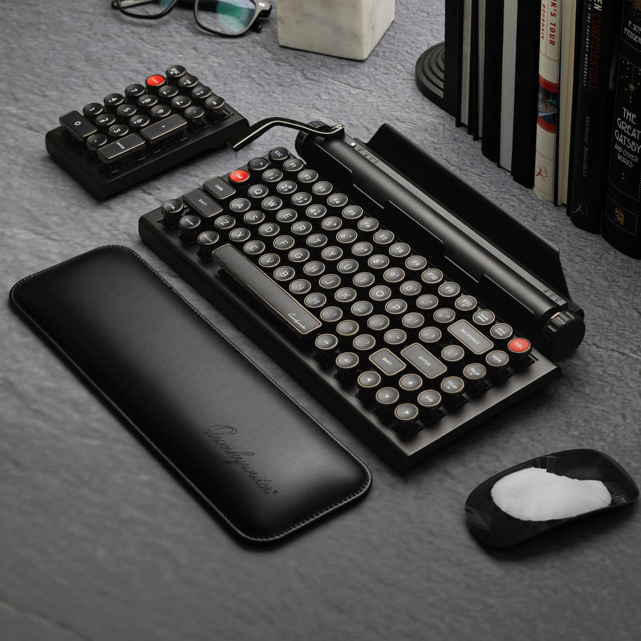 Qwerkywriter typewriter keyboard best in class premium all aluminum body in dark chrome hero image on grey stone slab background on a desk Alternate angle view