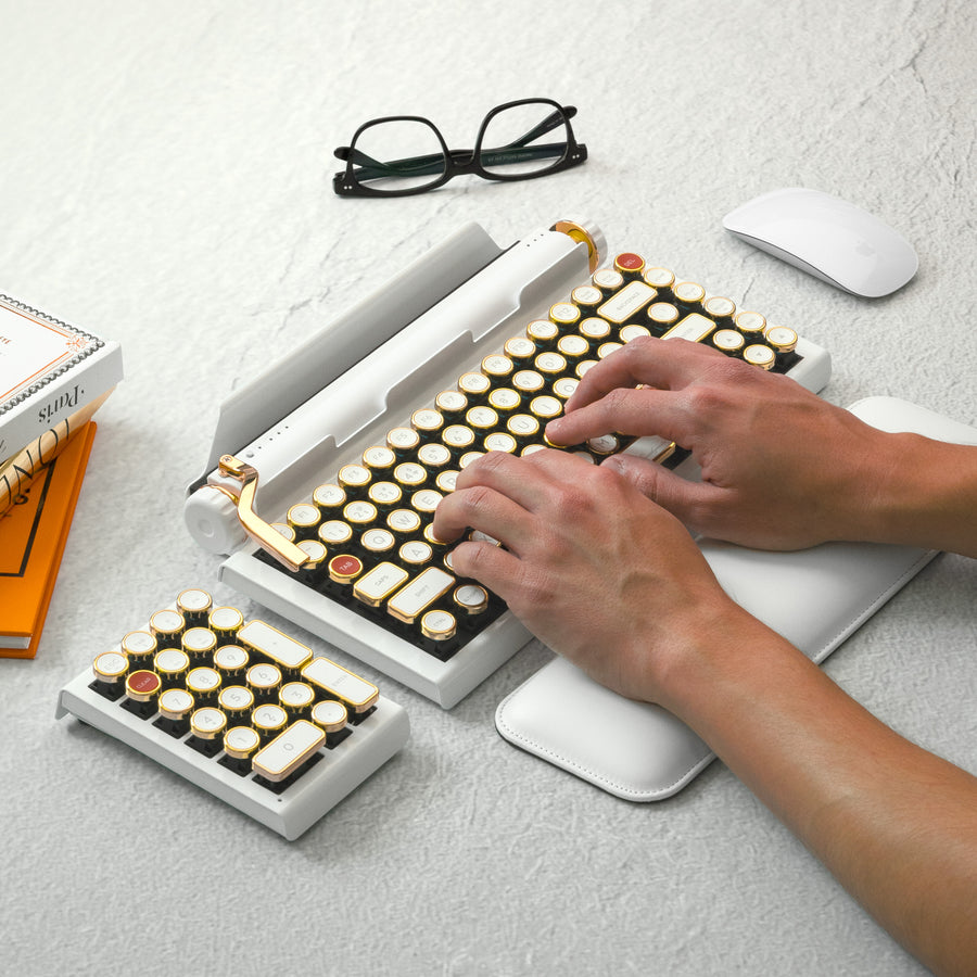 Qwerkywriter typewriter keyboard best in class premium all aluminum body in white gold on light background typing with glasses and books