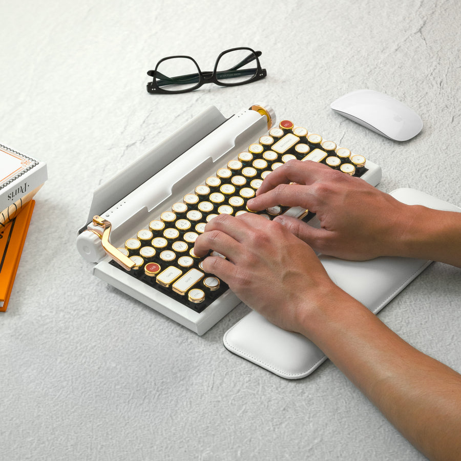 Qwerkywriter typewriter keyboard best in class premium all aluminum body in white gold on light background typing with glasses and books