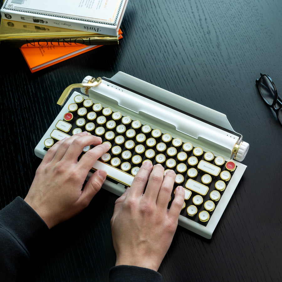 Qwerkywriter typewriter keyboard best in class premium all aluminum body in white gold on dark wood background typing with glasses and books