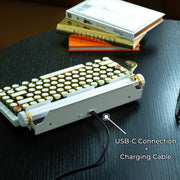 Qwerkywriter typewriter keyboard best in class premium all aluminum body in white gold on dark wood background with USB C charging and connection cable with dongle